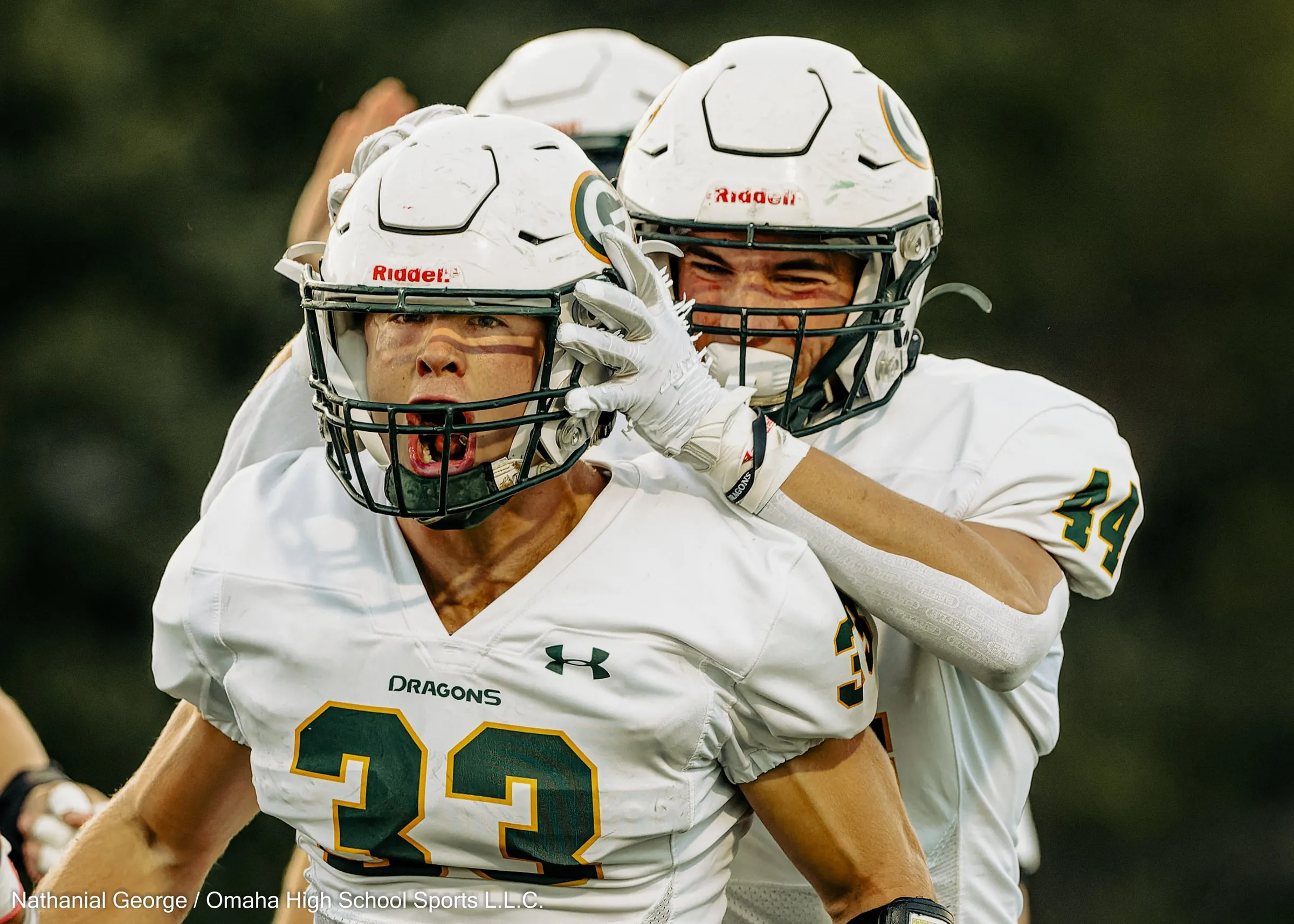 A Dragons defender in white, number 33, shouts through his face mask as a teammate, number 44, slaps the side of his helmet in celebration.
